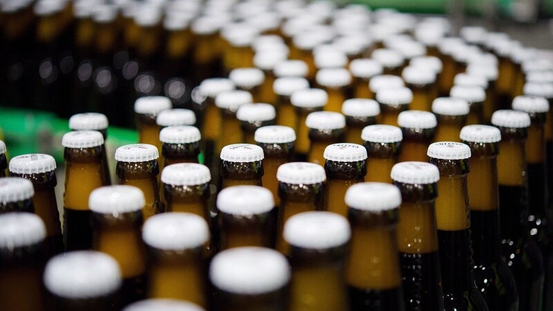 Bierflaschen mit Kronkorken laufen durch die Produktion einer Brauerei über die Förderbänder einer Befüllungsanlage.