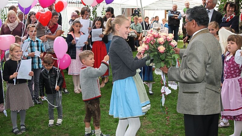 Pfarrer Joy inmitten der Kinder bei ihren Gratulationen mit Luftballons und Blumen.