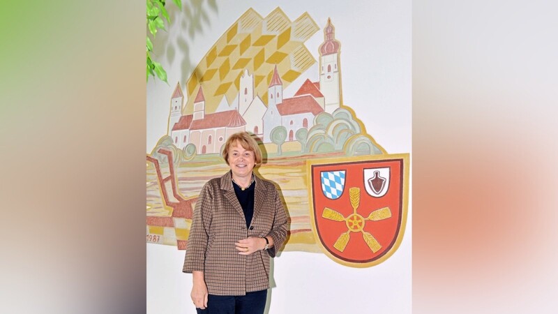 Bürgermeisterin Barbara Unger im Rathaus vor dem Gemeindewappen und der Ortsansicht von Feldkirchen.