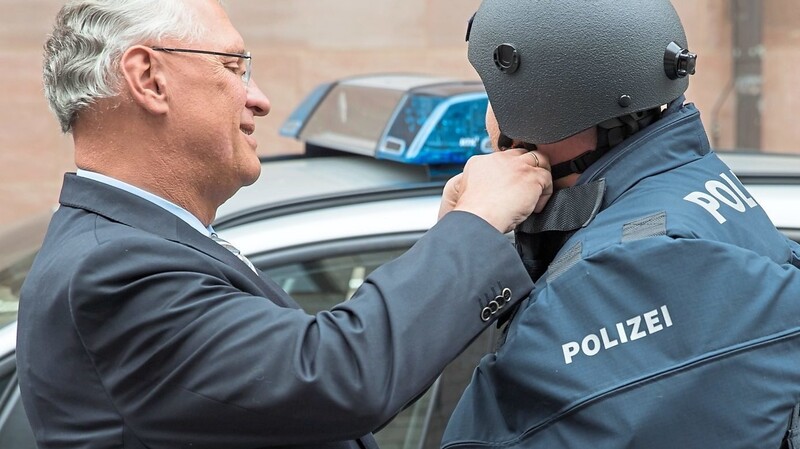 Innenminister Joachim Herrmann (l., CSU) hilft einem Polizisten in seine schwere Schutzausrüstung. Modernes Equipment soll die Beamten vor immer mehr Übergriffen schützen.