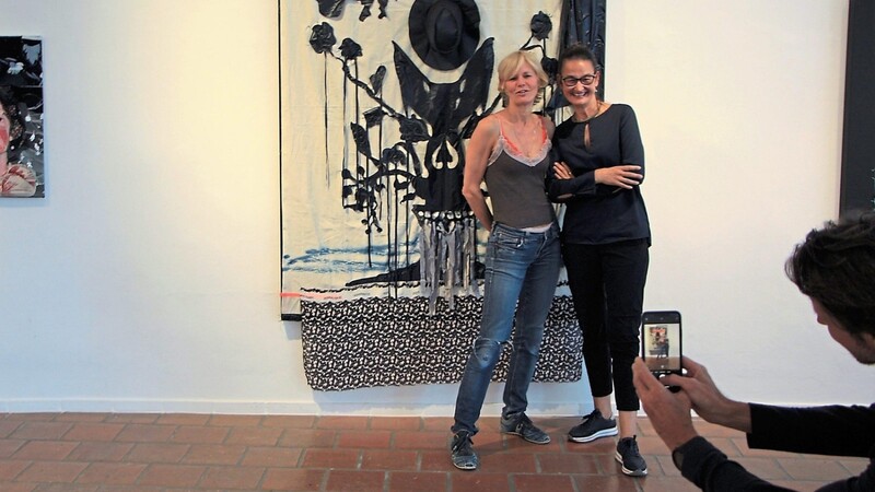 Martina Salzberg (links) und Galerieleiterin Anjalie Chaubal posieren vor einem der Werke in der Ausstellung. Darin hat die Künstlerin unter anderem einen Hut verarbeitet.