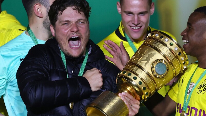 Edin Terzic (M.), Dortmunds Cheftrainer, hält den DFB-Pokal im Arm und feiert mit der Mannschaft. Ob er auch kommende Saison noch beim BVB tätig ist, scheint fraglich.
