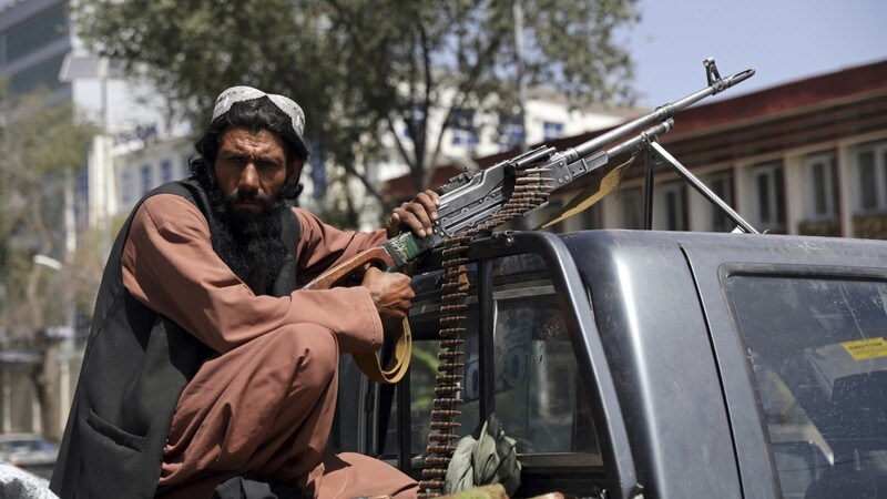 Ein Taliban-Kämpfer sitzt auf dem Rücksitz eines Fahrzeugs mit einem Maschinengewehr vor dem Haupttor zum Präsidentenpalast.