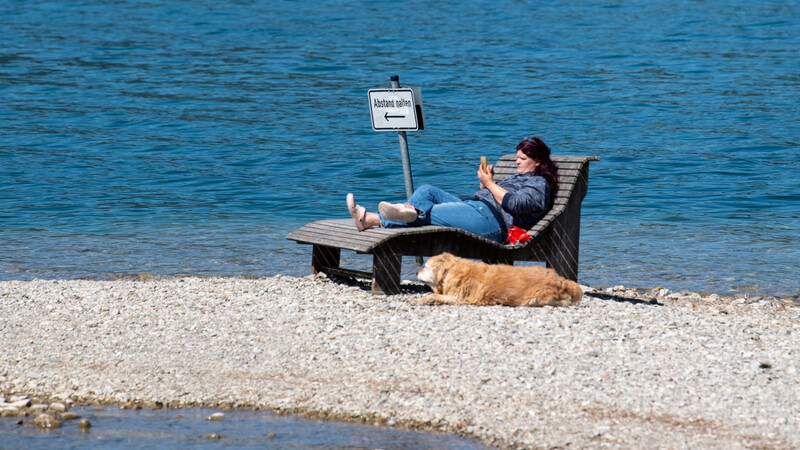Am Tegernsee liegt eine Frau mit ihrem Hund ganz allein auf einer Bank, ...