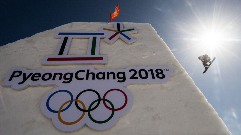 Ein Snowboarder in Aktion. Im Vordergrund ist das Logo und der Schriftzug der Olympischen Spiele zu sehen.