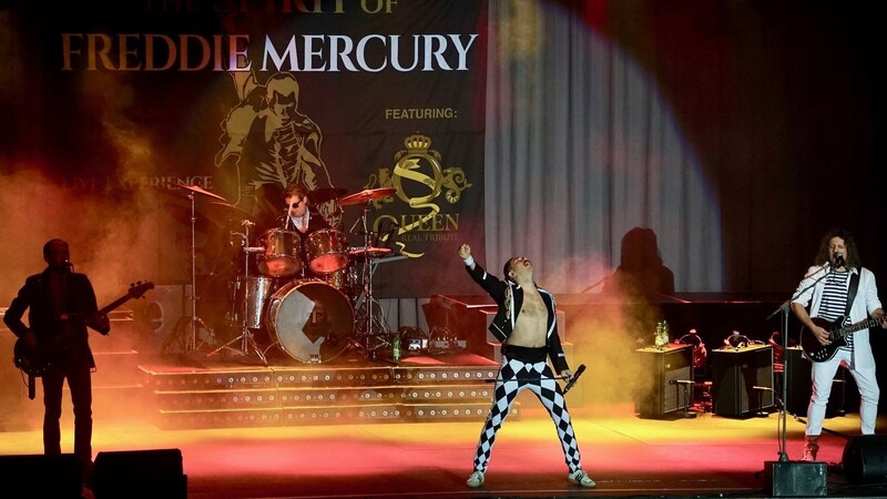 In einer seiner typischen Bühnenposen zeigt sich "Freddie Mercury" inmitten seiner Musiker.