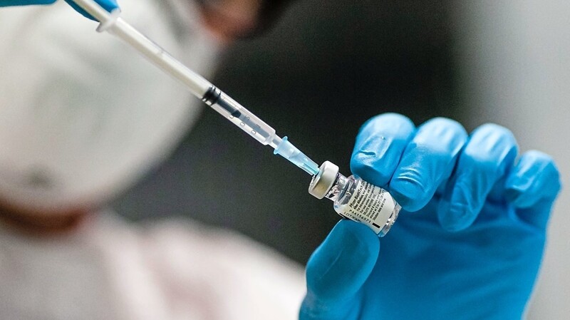 Eine Mitarbeiterin in einem Impfzentrum zieht mit einer Kanüle das Vakzin aus einer Glasampulle auf.