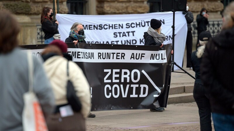 Teilnehmer einer "ZeroCovid"-Kundgebung am 2. April auf dem Hamburger Rathausmarkt zeigen Plakate mit der Aufschrift "Gemeinsam runter auf Null - Zero Covid" und "Menschen schützen statt Wirtschaft und Konzerne".