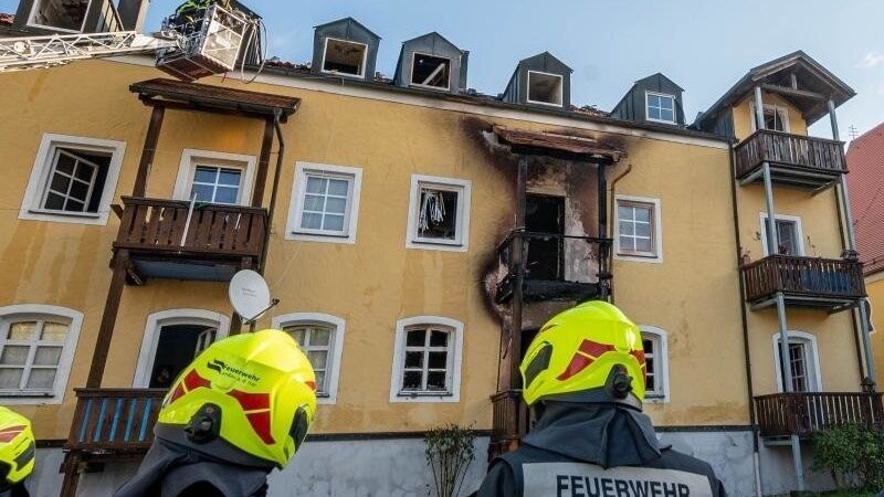 Feuerwehrmänner stehen vor einem ausgebrannten Mehrfamilienhaus.