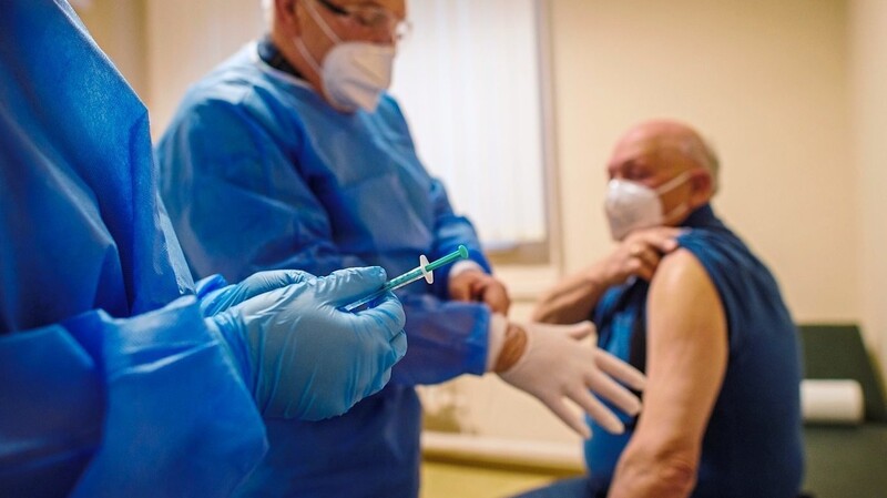 Eine Helferin reicht eine Spritze mit einer Impfdosis von Biontech/Pfizer an einen Arzt weiter.