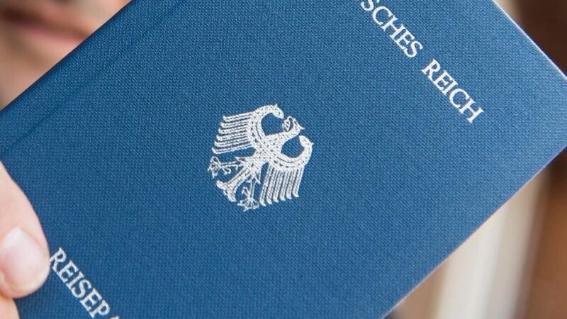 Ein Mann hält ein Heft mit dem Aufdruck "Deutsches Reich Reisepass" in der Hand.