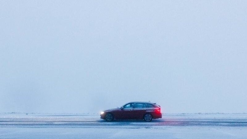 Ein Auto fährt bei dichtem Nebel über eine schneebedeckte Straße.