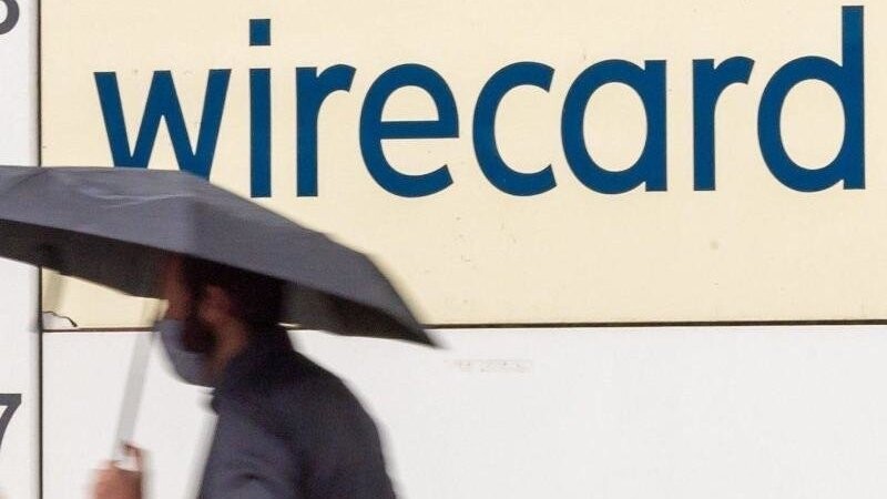 Ein Mann mit Regenschirm geht vor dem Schriftzug der insolventen Firma Wirecard an der Fassade des Unternehmens in Aschheim bei München vorbei. Foto: Peter Kneffel/dpa/archiv
