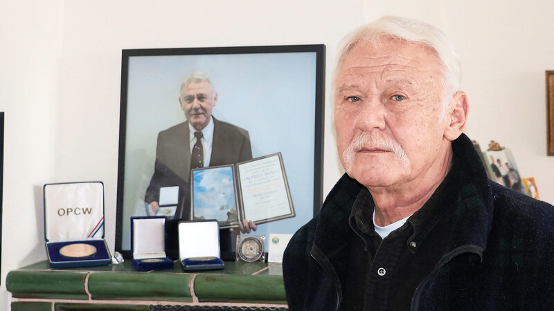 Horst Reeps vor einem Bild von sich mit der Nobelpreismedaille und der Urkunde.
