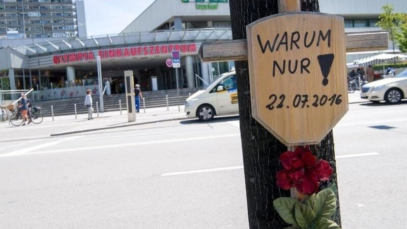 Ein Holzkreuz mit der Aufschrift "Warum nur! - 22.07.2016" hängt vor dem Eingang zum Olympia-Einkaufszentrum (OEZ).