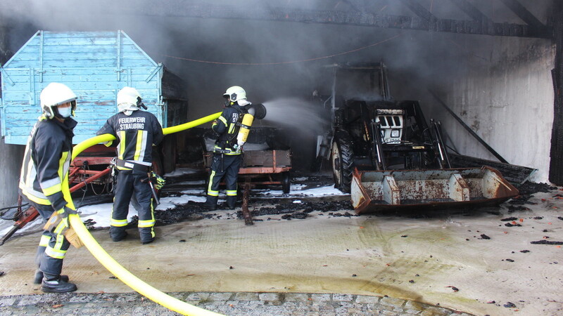 Mitglieder der Freiwilligen Feuerwehr löschen den Traktor in der Garage, von dem der Brand wohl ausging.