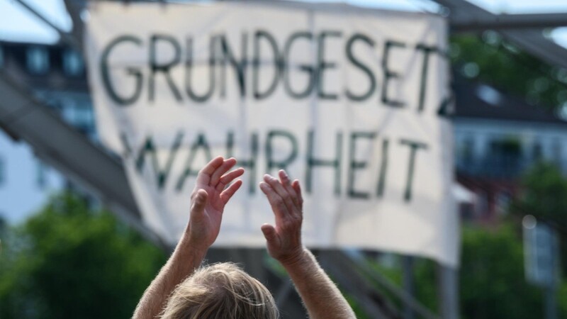 Ein Demonstrant klatscht bei einer der zahlreichen Demonstrationen in Deutschland vor einem Plakat mit dem Slogan "Grundgesetz Wahrheit".