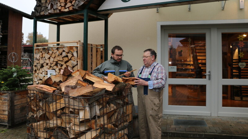Forstrat Markus Riebler von der Bayerischen Landesanstalt für Wald und Forstwirtschaft (LWF) und Mathias Bauer vor einer Gitterbox mit aufgeschütteten Scheitholz.