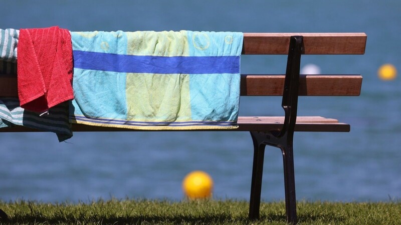 Handtücher hängen am Ufer des Strandbades zum Trocknen über einer Bank.