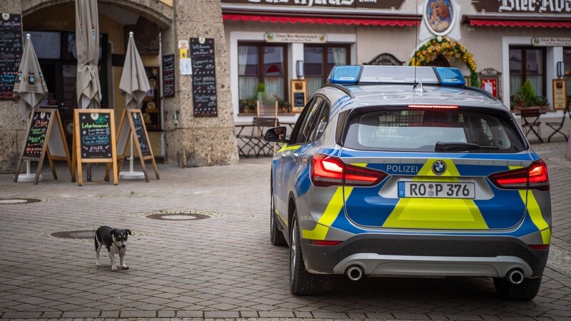 Ein Streifenwagen der Polizei fährt zur Kontrolle der Maskenpflicht durch die leere Innenstadt von Berchtesgaden und hält neben einem Hund.