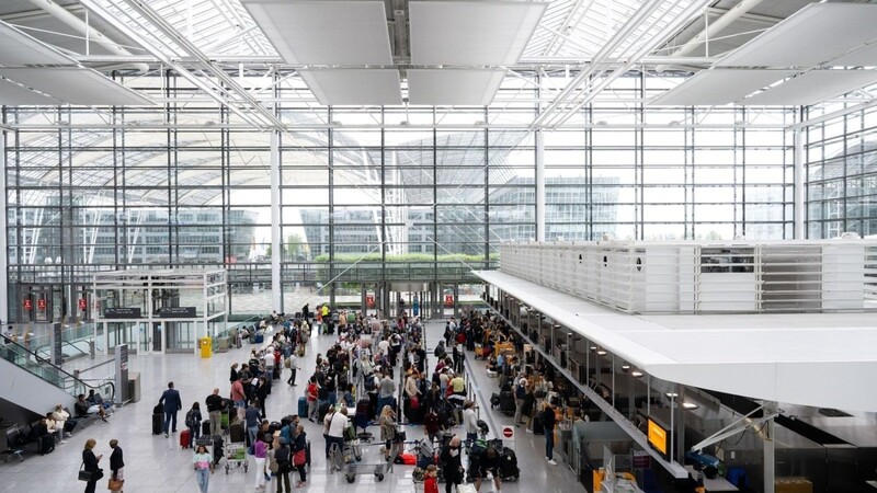 Passagiere stehen am Flughafen München an Check-in-Schaltern.