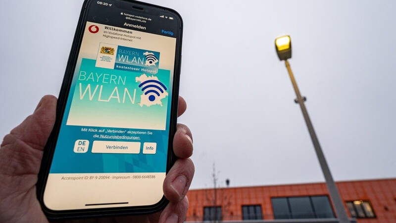 Ein Handy zeigt die Internetseite vom BayernWLAN-Netz neben einer Straßenlaterne. Die erste bayerischen WLAN-Hotspot in einer Straßenlaterne wurde am Technologie Campus Parsberg-Lupburg freigeschaltet.