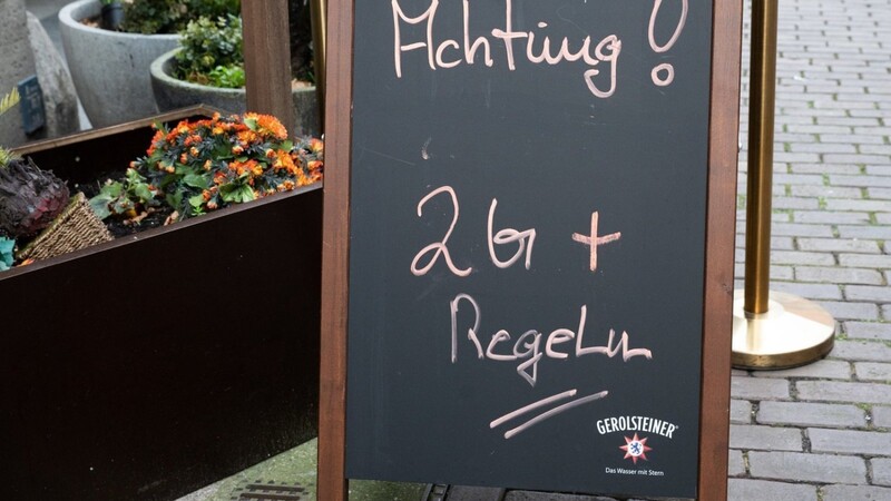 Ein Hinweisschild mit Aufschrift "Achtung! 2G+ Regel" steht vor einem Restaurant in der Innenstadt.
