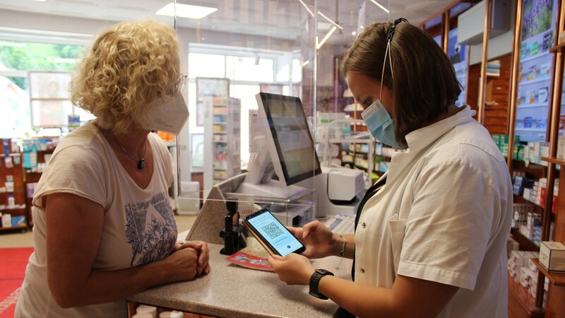 Eine Mitarbeiterin der Apotheke erklärt einer Kundin, wie man den digitalen Impfnachweis scannt.