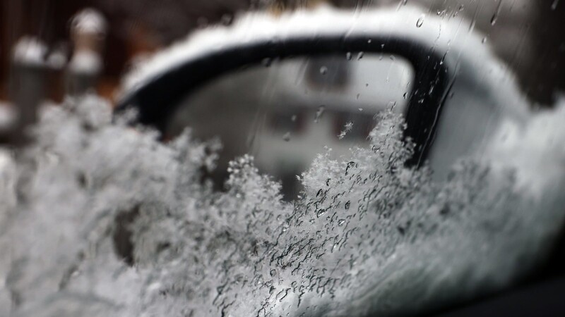 Der Außenspiegel eines Autos ist hinter einer teilweise mit Schnee bedeckten Autoscheibe zu sehen.