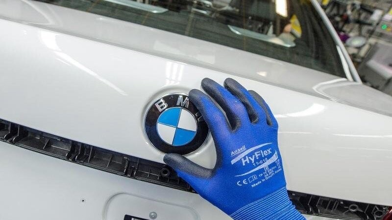 Ein Mitarbeiter montiert im BMW-Werk in Dingolfing ein BMW-Emblem auf den Kofferraumdeckel eines Fahrzeugs.
