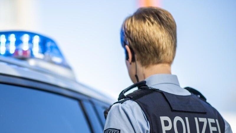 Eine Polizistin steht neben einem Streifenwagen mit eingeschaltetem Blaulicht.