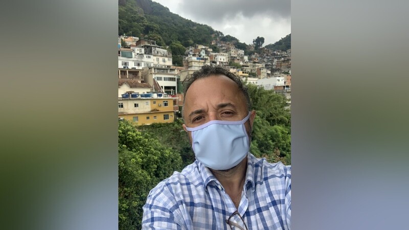 Marcelo Salomao mit Mund-Nasen-Schutz auf dem Balkon seiner Wohnung. Im Hintergrund die nahe gelegene Favela.