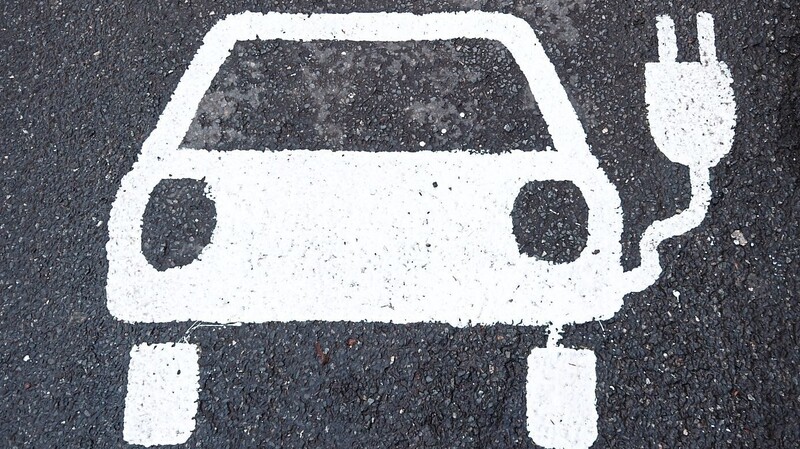 Ein Symbol für ein Elektroauto markiert einen Parkplatz neben einer E-Ladesäule. Der Verkehr soll klimafreundlicher werden.