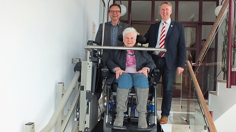 Zufrieden nach dem Besuch im Bürgermeisterzimmer fährt Barbara Sixt mit dem neuen Treppenlifter wieder nach unten. Begleitet wird sie dabei von (li.) Bürgermeister Franz Wittmann und dem Behindertenbeauftragten des Landkreises Helmut Plenk.