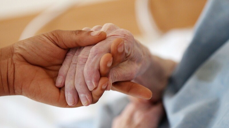 Eine Pflegerin hält einem Altenheim die Hand einer Bewohnerin.