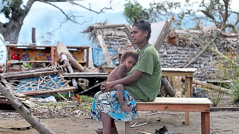 Eine Frau mit ihrem Kind blickt auf die Trümmer ihrer Behausung.
