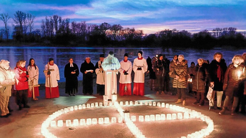 Die Geistlichkeit und die Gläubigen hinter einem Kreuz aus Kerzen und vor den Wogen der Donau.