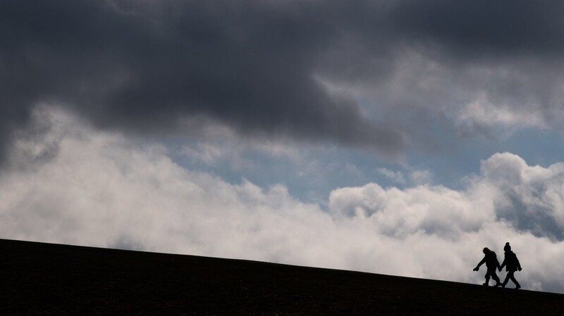Zwei Kinder laufen auf einen Hügel am Kronsberg, während bei stürmischen Wetter dunkle Wolken am Horizont vorüberziehen.
