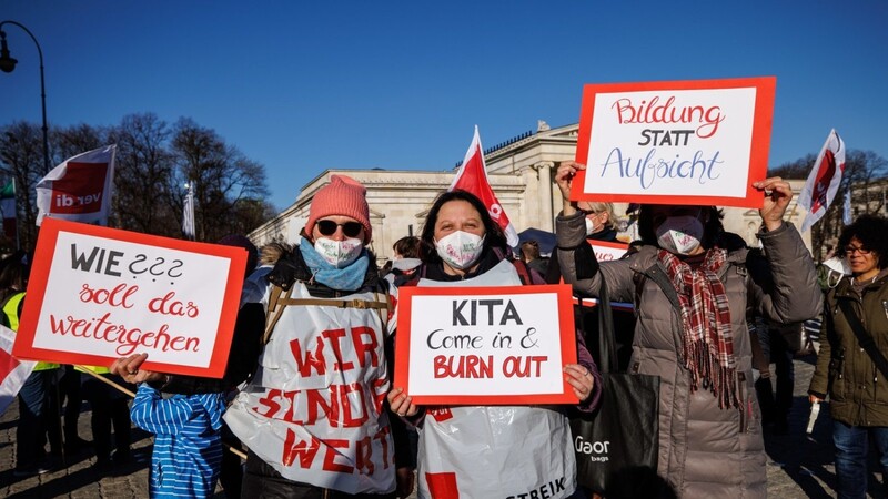 Demonstrationsteilnehmerinnen halten während einer Verdi-Kundgebung von Beschäftigten im Sozial- und Erziehungsdienst auf dem Königsplatz Schilder mit den Aufschriften "Wie??? soll das weitergehen", "Kita - Come in & Burn out" und "Bildung statt Aufsicht".