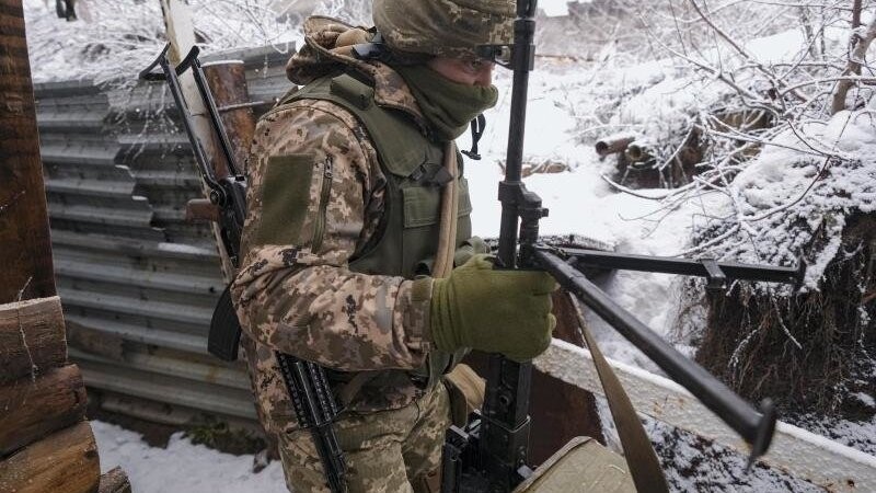 Ein ukrainischer Soldat trägt in einem Graben an der Frontlinie in der Ostukraine ein schweres Maschinengewehr.