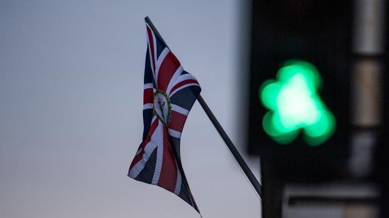 Vor einer wehenden Britischen Flagge leuchtet eine Grüne Ampel.