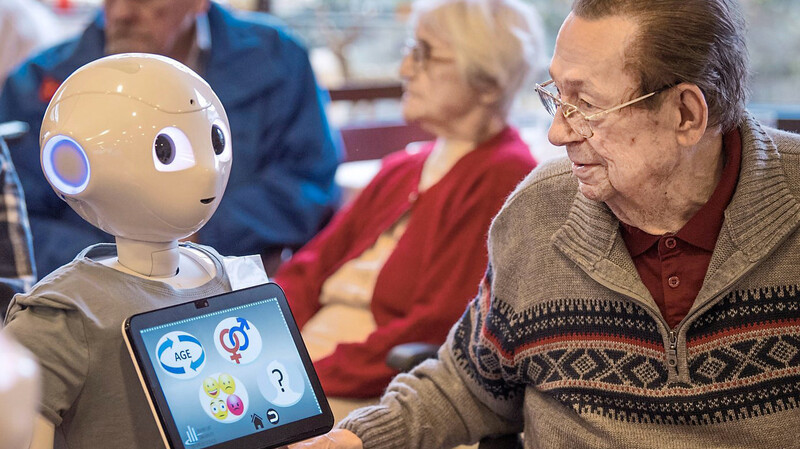 Auf Tuchfühlung mit dem Roboter "Pepper" geht ein Bewohner eines Alten- und Pflegeheims während einer Infoveranstaltung in Frankfurt am Main. Roboter und andere Hilfen mit Künstlicher Intelligenz sollen künftig immer mehr in der Medizin und Pflege eingesetzt werden.