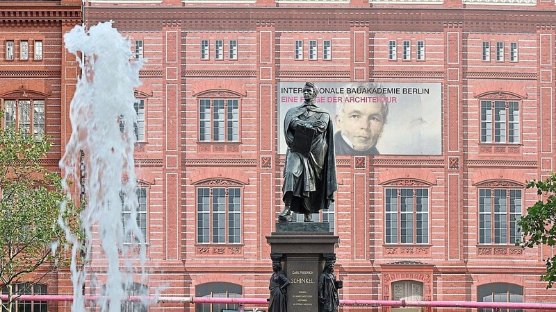 Eine Schaufassade, bestehend aus Mauerteilen und bedruckten Planen, zeigte bis vor Kurzem das einstige Aussehen der Berliner Bauakademie. Davor ist ein Denkmal von Karl Friedrich Schinkel zu sehen.