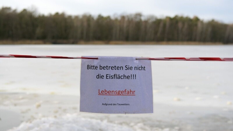 Ein Schild warnt am Ufer eines Sees vor dem Betreten der Eisfläche.