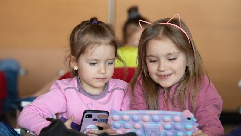 Zwei kleine Mädchen aus der Ukraine spielen in einer Notunterkunft an einem Tablet.