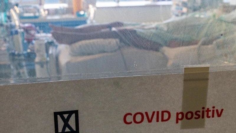 Ein schwer an Covid-19 erkrankter Patient liegt hinter einem Schild mit dem Hinweis "Covid positiv" in einem Isolierzimmer auf der Corona-Intensivstation im Universitätsklinikum in Halle/Saale.