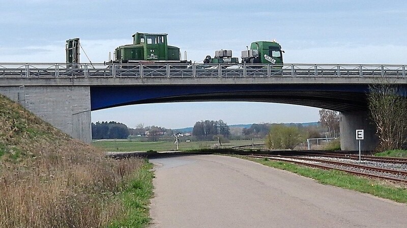 Das Bockerl fährt auf einem Tieflader auf der B 15 neu-Brücke genau über der Bahnlinie am Anschluss Eichbühl in Schierling, wo es normalerweise zwischen Eggmühl und Langquaid entlang verkehrt