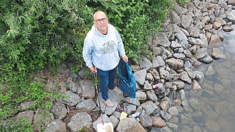Mit einem Greifer pflückt Thomas Thalhammer Plastikmüll von den Ufersteinen.