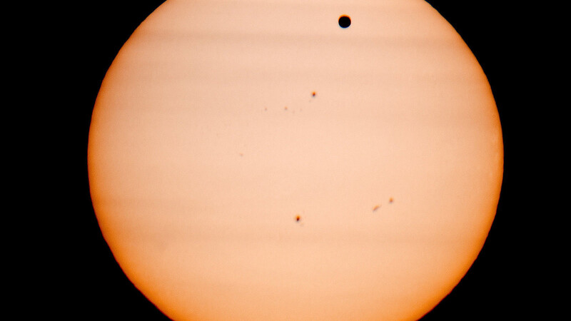Blick durchs Teleskop: Der Planet Venus (als schwarzer Punkt oben im Bild) durchläuft die Sonne. Die anderen dunklen Stellen sind Sonnenflecke auf der Oberfläche der Sonne.