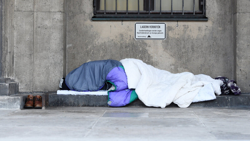 Ein Obdachloser schläft in Decken und Schlafsäcke gehüllt im Freien. Im Winter ist das gefährlich, bayerische Kommunen rüsten sich deshalb und bieten teils mehr Plätze in Notunterkünften.